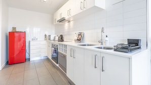 Una cocina moderna con armarios blancos, un refrigerador rojo, electrodomésticos de acero inoxidable y un escurreplatos negro.