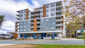 A multi-story residential building with balconies, a ground-level commercial area, and a parking lot. - 2BR Apt in the heart of the Gungahlin Town Centre! (Gungahlin)