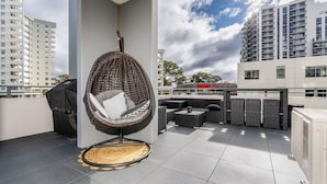 A rooftop terrace with a hanging chair, outdoor seating, and a view of the cityscape. - 2BR Apt in the heart of the Gungahlin Town Centre! (Gungahlin)