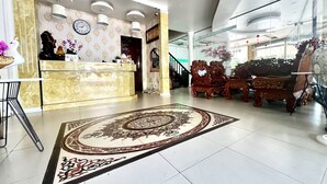 Un hall d’hôtel moderne avec un comptoir d’accueil, des meubles en bois richement décorés et un tapis à motifs.