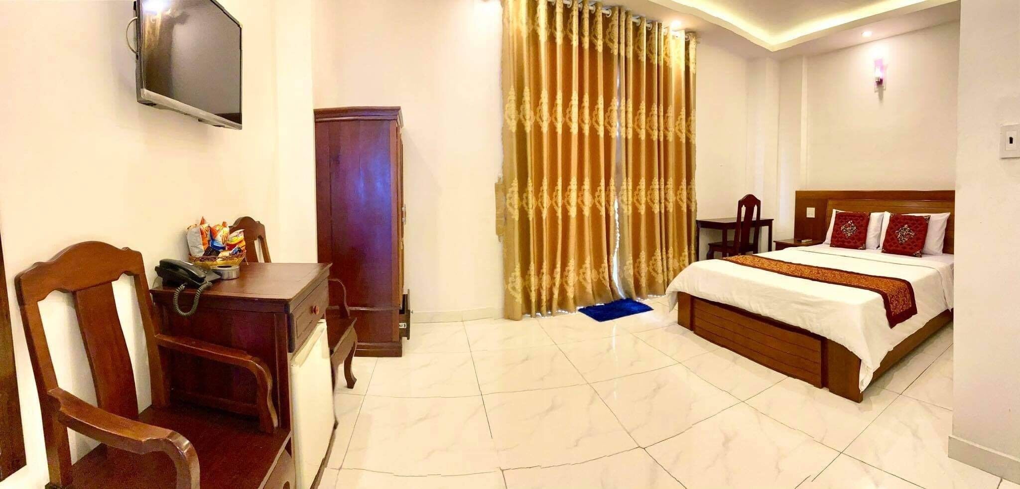 A hotel room with a bed, a desk with a telephone, a TV mounted on the wall, and a curtain.
