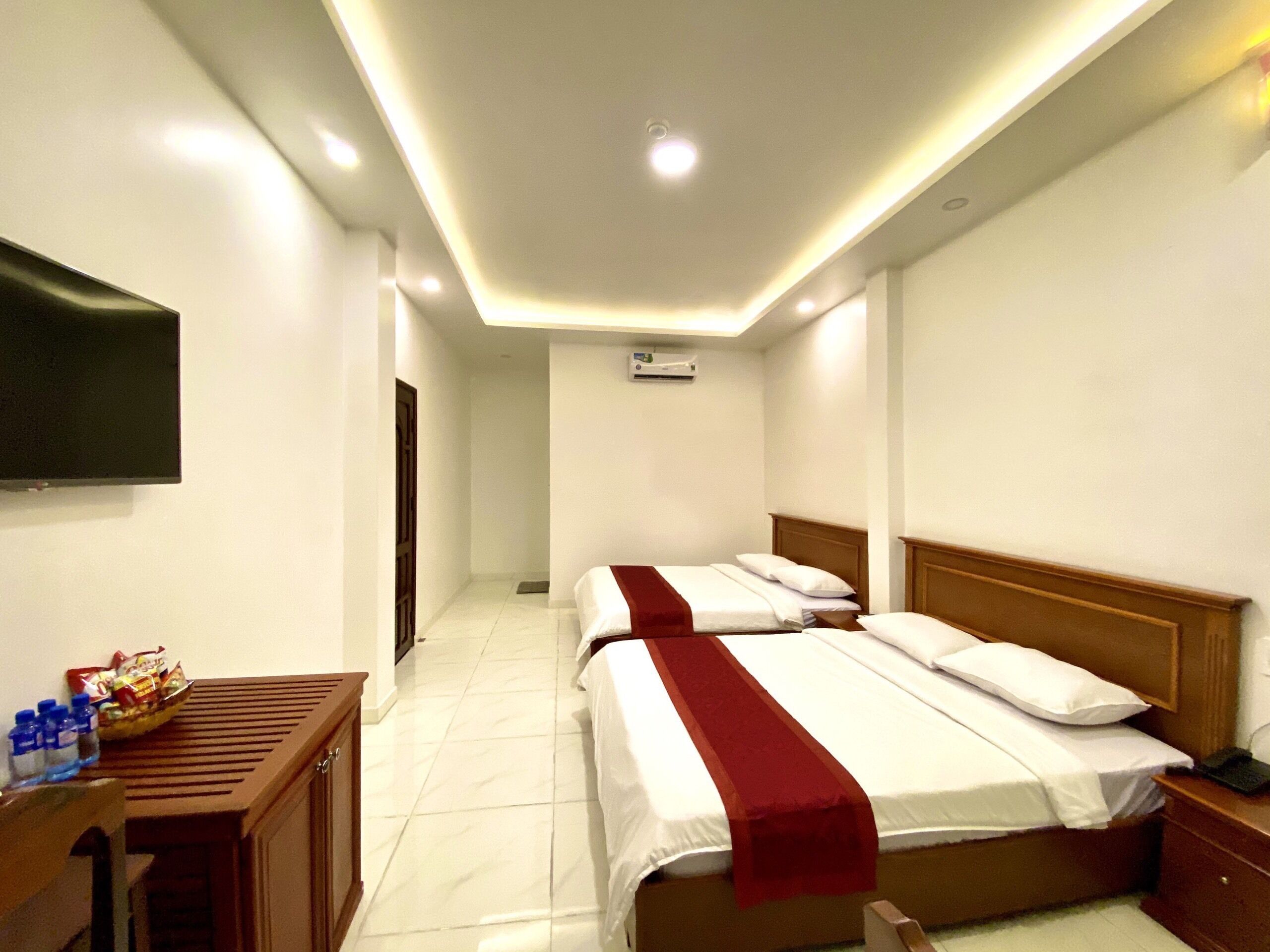 A hotel room with two beds, a desk, a TV, and an air conditioning unit.