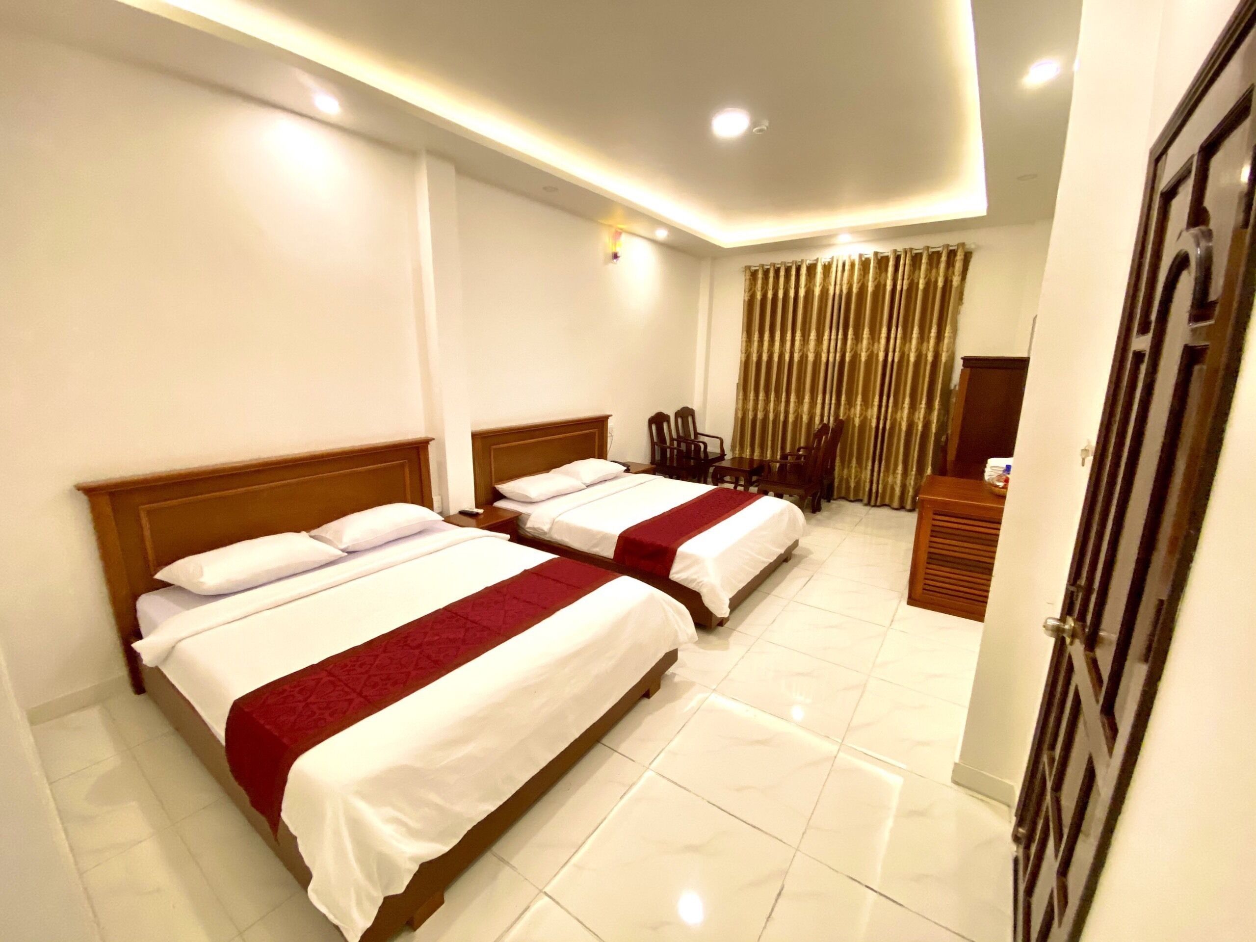 A hotel room with two beds, a desk, chairs, and a curtain.