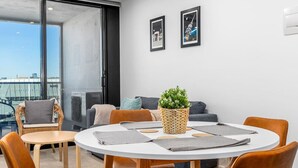 Een moderne woonkamer met een ronde tafel, zachte zitplaatsen, een groot raam en twee ingelijste foto's aan de muur.
