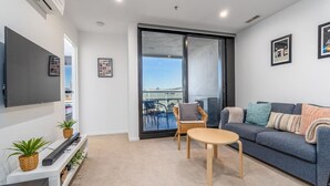 Een moderne woonkamer met een flatscreen televisie, een bank, een klein rond tafeltje en een balkon met uitzicht.