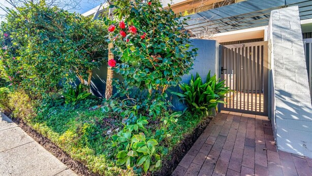 Un jardín ajardinado con diversas plantas y una entrada porticada a un edificio.