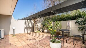 Un patio con pérgola, mobiliario exterior y plantas en macetas.