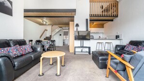 A modern living room with a sofa, coffee table, and a TV. There is a staircase leading to an upper level with a kitchen area. - 3BR Loft Apt 1min to Kingston Foreshore! (Kingston)