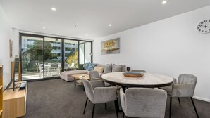 Un salón moderno con una mesa de comedor redonda, sillas tapizadas en gris, un sofá y un amplio ventanal con vistas a la ciudad.