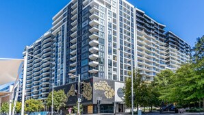 A modern high-rise building with multiple balconies, a prominent entrance with a mosaic design, and a clear blue sky in the background. - Modern 2BR APT in Highgate Executive Apartment (Canberra)