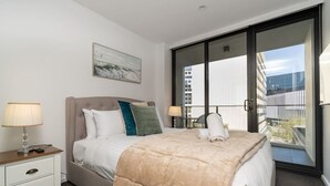 Un dormitorio con cama, mesitas de noche, una ventana con vistas y un cuadro en la pared.