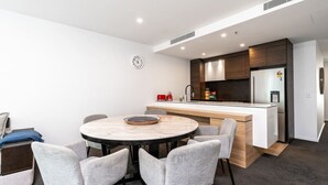 Una cocina moderna con una isla central, un área de comedor con una mesa redonda y sillas, y un reloj visible en la pared.