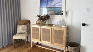 A living room with a wooden cabinet, a framed picture of a beach, a chair, and a grey curtain. - Lavish Home 4mins to the beach Pet- Friendly House (Bawley Point)