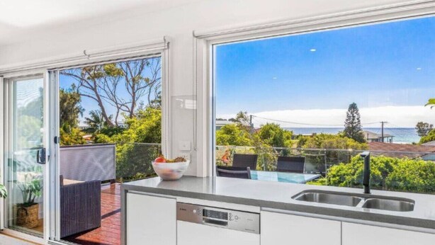 A modern kitchen with large windows, a view of the sea, and outdoor seating. - Lavish Home 4mins to the beach Pet- Friendly House (Bawley Point)
