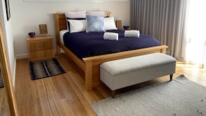 A modern bedroom with a wooden bed, a bench, a nightstand, and a window with curtains. - Lavish Home 4mins to the beach Pet- Friendly House (Bawley Point)