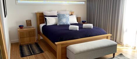 Une chambre moderne avec un lit en bois, un banc, une table de chevet et une fenêtre avec des rideaux.