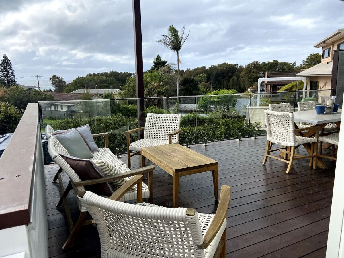 Une terrasse extérieure couverte, aménagée avec des meubles en osier et une table en bois, qui offre une vue sur un paysage luxuriant.