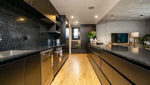 A modern kitchen with dark cabinetry, a wooden floor, and a central island. - Onyx Apt · Onsite EV Charger · 5mins to Foreshore (Kingston)