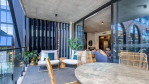 A modern outdoor seating area with wicker furniture, a round table, and a glass balustrade overlooking a cityscape. - Onyx Apt · Onsite EV Charger · 5mins to Foreshore (Kingston)