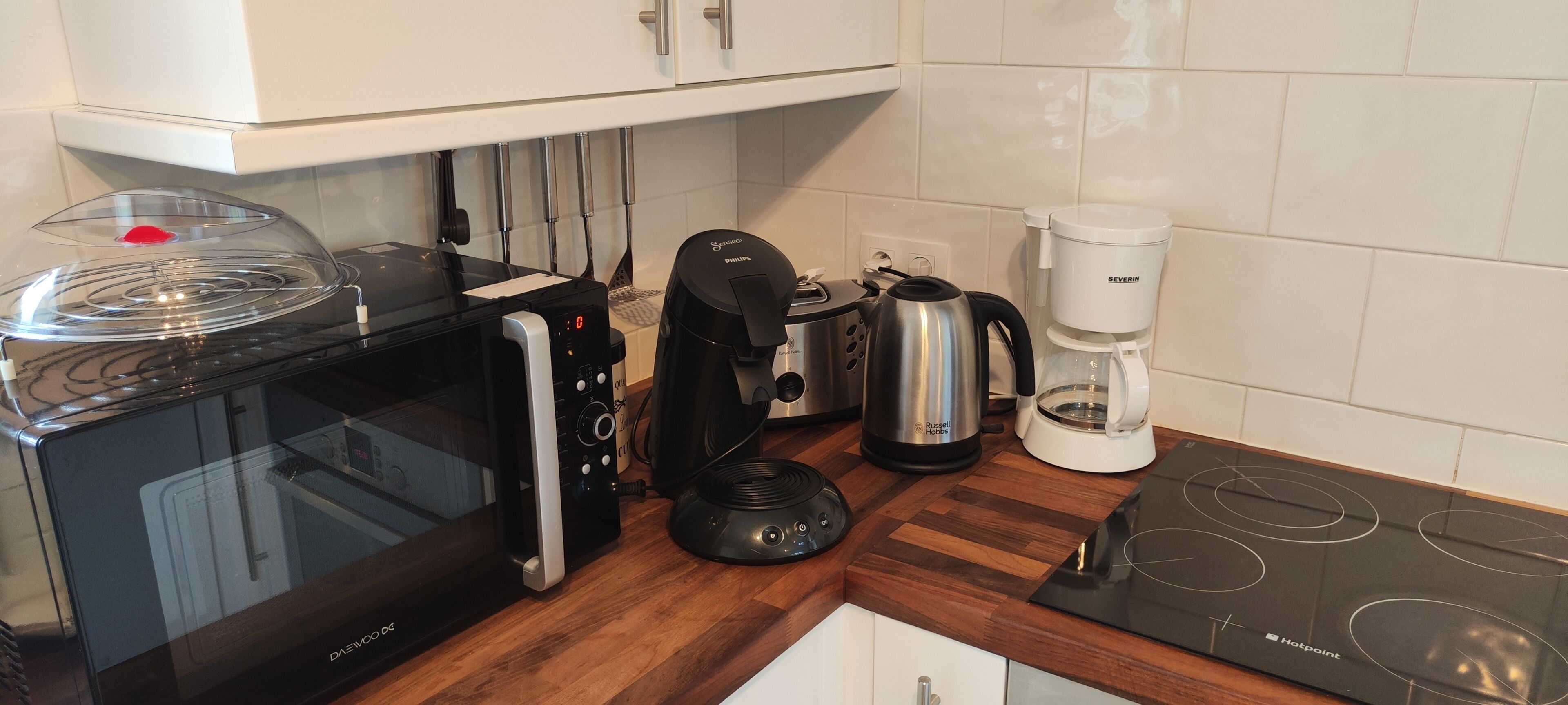 A compact kitchen with a microwave, coffee maker, and electric kettle on a wooden countertop.