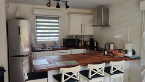 A kitchen with a wooden island, white cabinets, a stainless steel refrigerator, and a microwave. - Appartement Accueillant Tout Proche mer (Clohars-Carnoët)