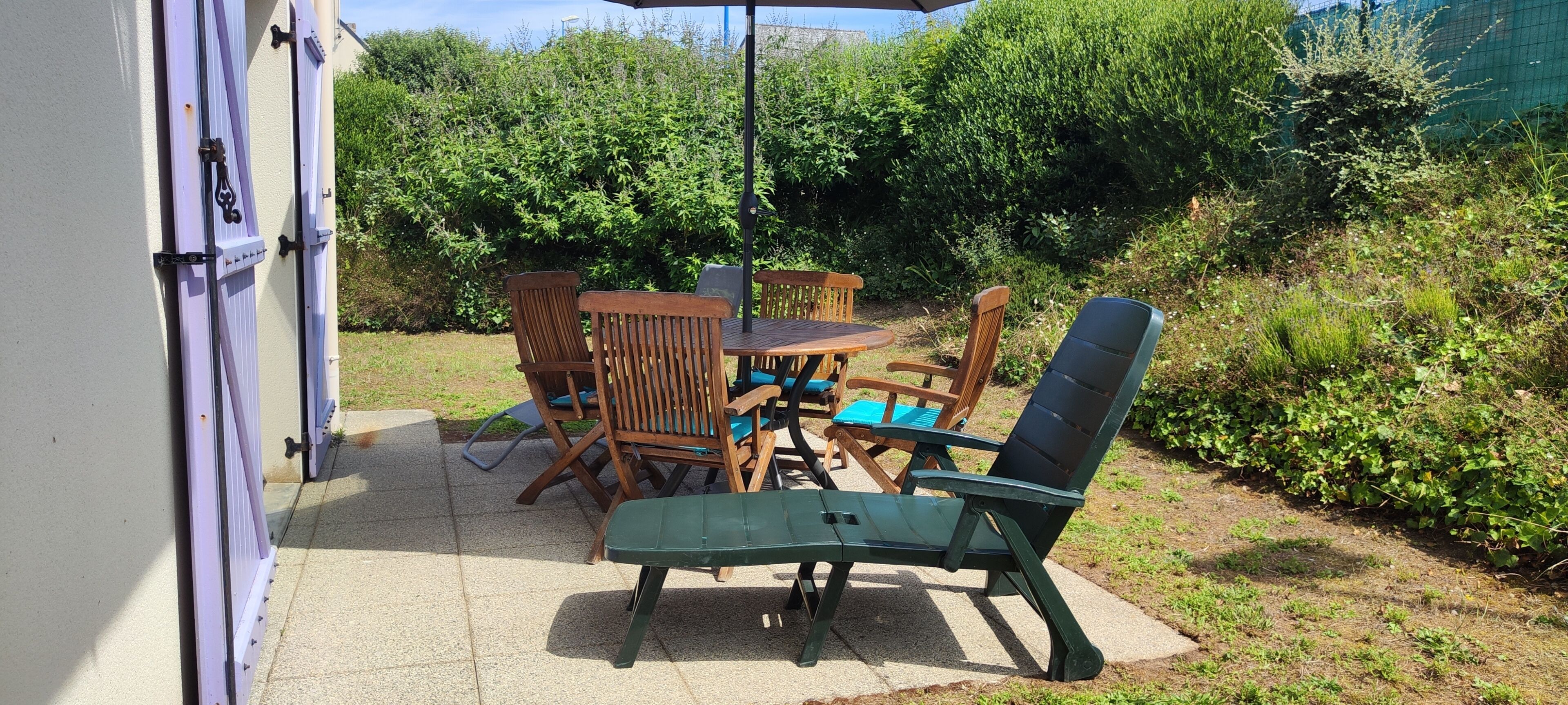 An outdoor patio with a table and chairs, surrounded by greenery.