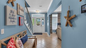 A modern living room with a wooden bench, a sofa, and a coffee table. There is a staircase with a glass railing leading to a door. - Spacious 3BR, Dreamy Backyard, 2 Pools, 6-Min Stroll to Beach + Free Tickets! (Santa Rosa Beach)