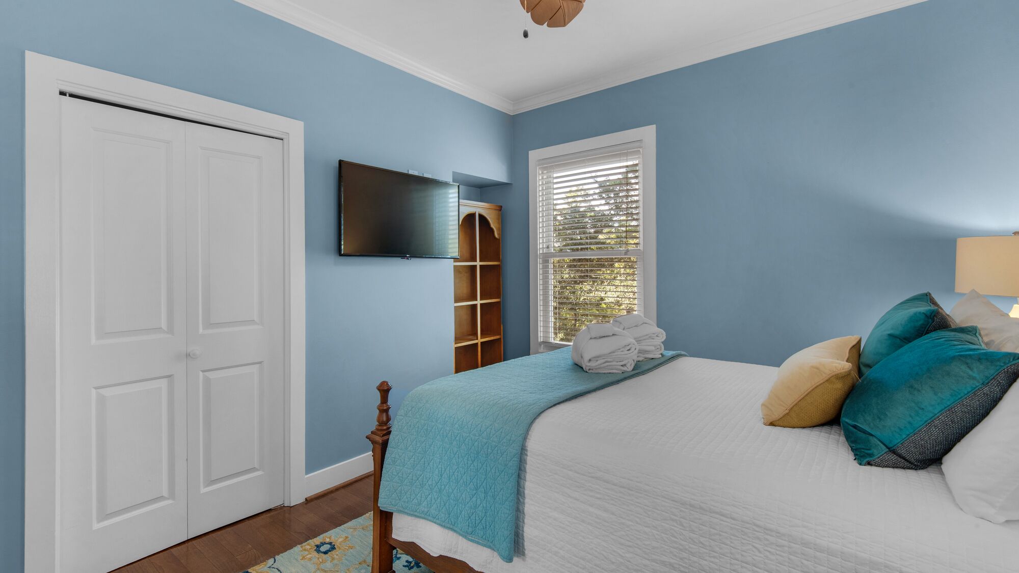 A bedroom with a bed, a TV, a window with blinds, and a door.