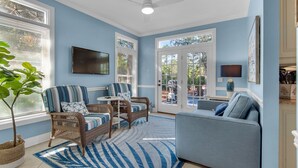 A living room with wicker furniture, a blue sofa, and a large window overlooking a backyard. - Spacious 3BR, Dreamy Backyard, 2 Pools, 6-Min Stroll to Beach + Free Tickets! (Santa Rosa Beach)