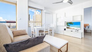 Ein modernes Wohnzimmer mit einer Couch, einem Couchtisch, einem Fernseher und einem Essbereich mit Stühlen und einem Tisch.