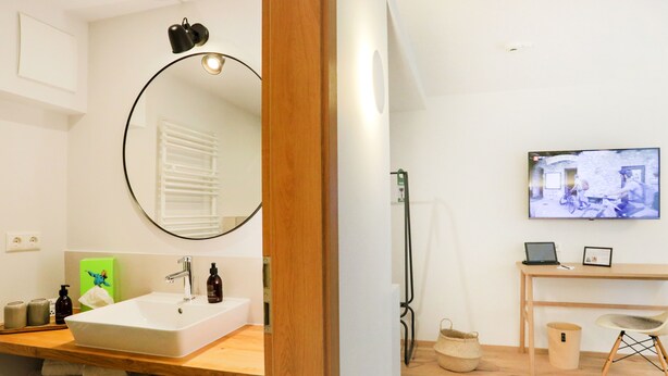 Une salle de bain moderne avec un grand miroir, un lavabo et un téléviseur fixé au mur.