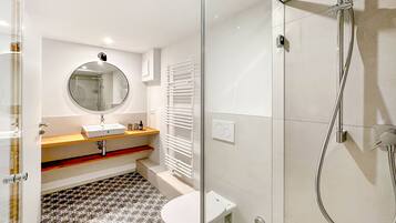 A modern bathroom with a glass shower enclosure, a round mirror above the sink, and a patterned floor.