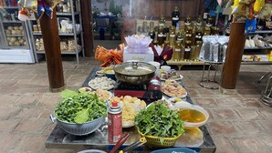 Une table sur laquelle se trouvent divers aliments, notamment des légumes, des nouilles et une casserole posée sur un réchaud portable.