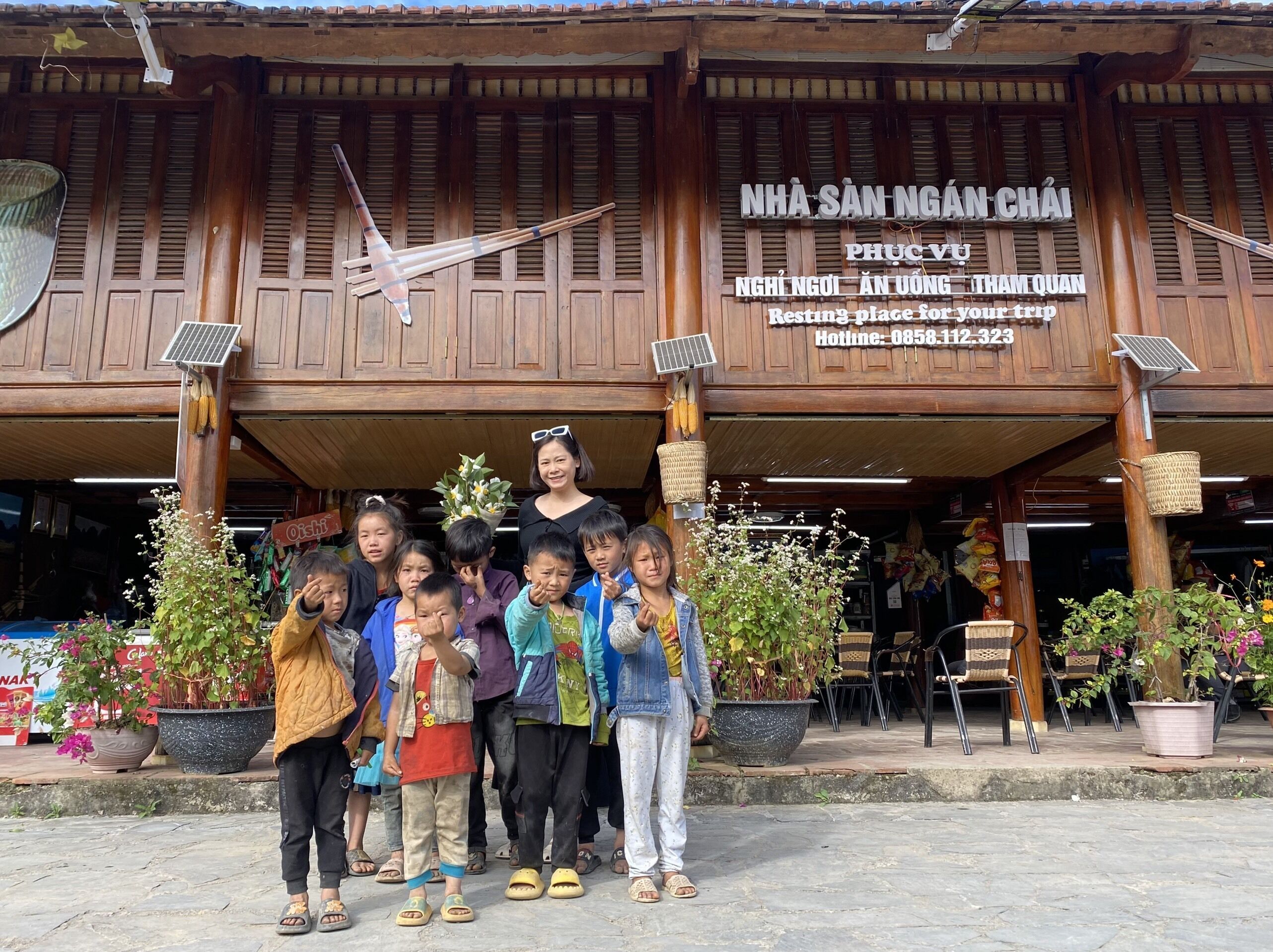 A wooden building with a sign reading "NHÃ SÃN NGÃN CHÃI PHUÃC VÃO NGHI NGÃI ÃN UONG THAM QUAN".