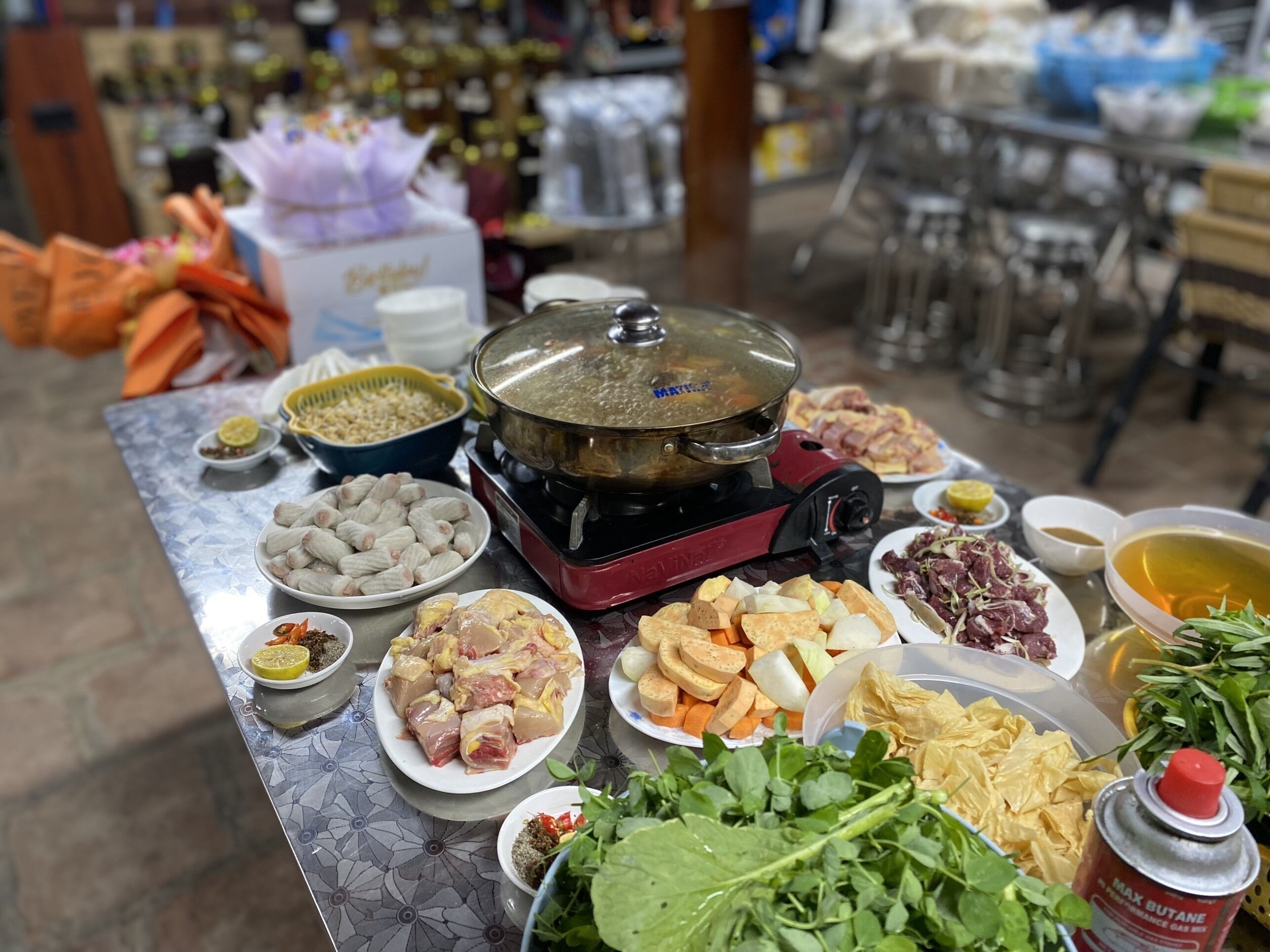 Una mesa con diferentes alimentos, como un caldo caliente, carnes crudas, verduras y salsas.