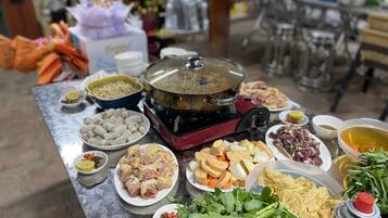 Una mesa con diferentes alimentos, como un caldo caliente, carnes crudas, verduras y salsas.