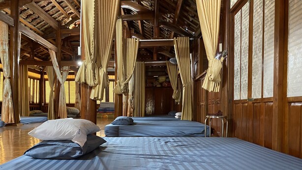 Une chambre avec deux lits, chacun doté de draps et d’oreillers à rayures. Les murs de la chambre sont en bois et le plafond est haut, avec des poutres apparentes.