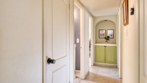A hallway with a white door, a green kitchen area, and a tiled floor.