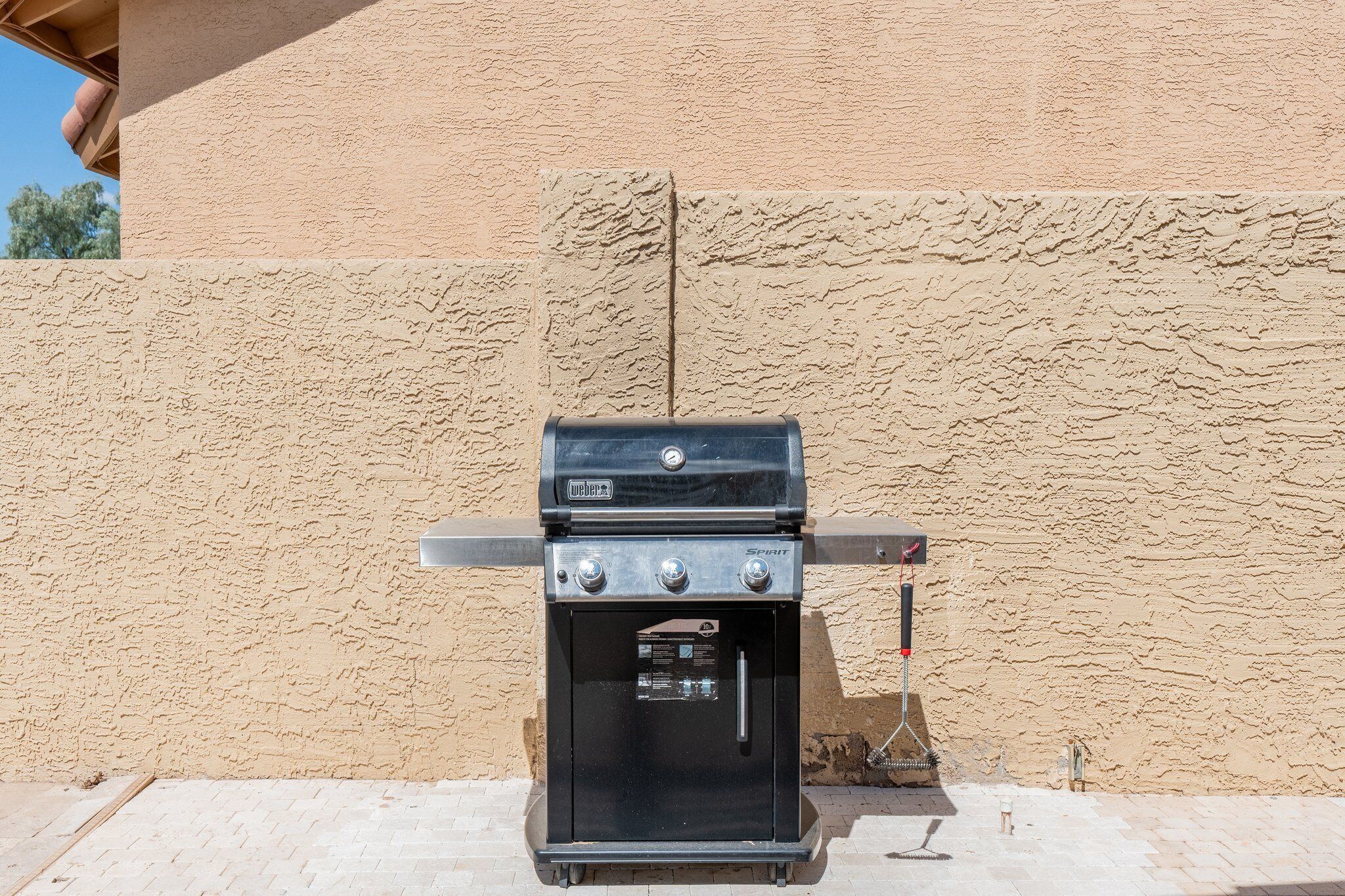 Una parrilla de gas Weber Spirit con un quemador lateral, ubicada frente a una pared beige con textura.