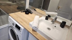 Une salle de bain moderne avec un plan de travail en bois, un lave-linge, un évier et un espace douche.