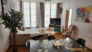 Une chambre moderne équipée d’un lit, d’une télévision, d’une table à manger avec des chaises et d’une grande fenêtre avec des rideaux.