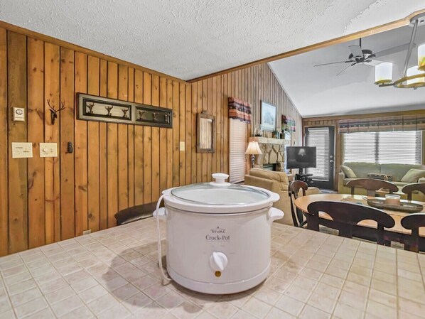 A kitchen with a white Rival Crock-Pot, wooden walls, a dining table with chairs, and a television. - Wabasso 1 Covered Parking Convenient Location WiFi (Snowshoe)