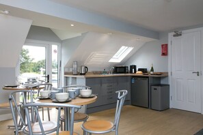 A modern kitchen with a dining area, featuring a skylight, a built-in oven, and a compact dishwasher.