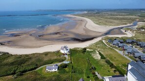 An aerial view of a coastal area with a sandy beach, a white house with a driveway, and a cluster of houses with sloped roofs. - Modern en-suite room in country Pub/Restaurant (1) with communal kitchen - Pass the Keys (Llanddona)