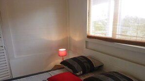Une chambre à coucher avec un lit, des oreillers, une table de chevet, une lampe et une fenêtre avec des stores.