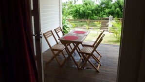 Une terrasse ouverte avec une table et des chaises en bois, un set de table rouge et une vue sur un jardin luxuriant.