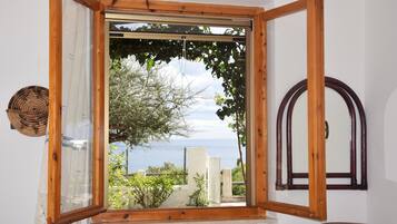 Ein Zimmer mit einem großen Fenster mit Holzrahmen, das auf einen Garten und ein Gewässer blickt.