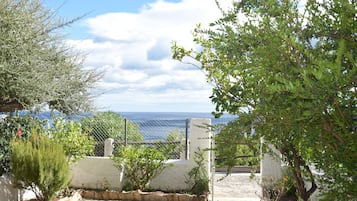 Ein gepflasterter Weg führt zu einem weißen Tor mit Blick auf das Meer.