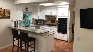 A kitchen with white cabinets, a granite countertop, a built-in oven, and a small island with bar stools. - Private pool, spa, waterfall, firepit, BBQ, tennis, gym, hiking trails, casino (Palm Desert)