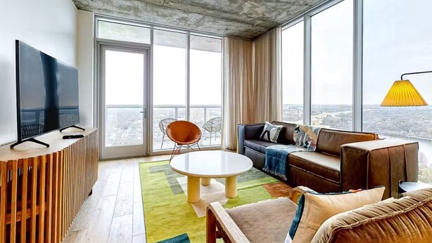 A modern living room with a large window, a sofa, a coffee table, and a TV on a wooden console.
